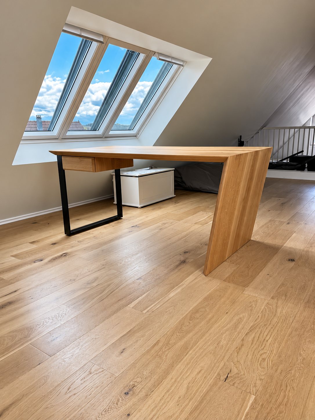 Bureau en bois clair à pied métallique noir sous les combles, sur un parquet en chêne