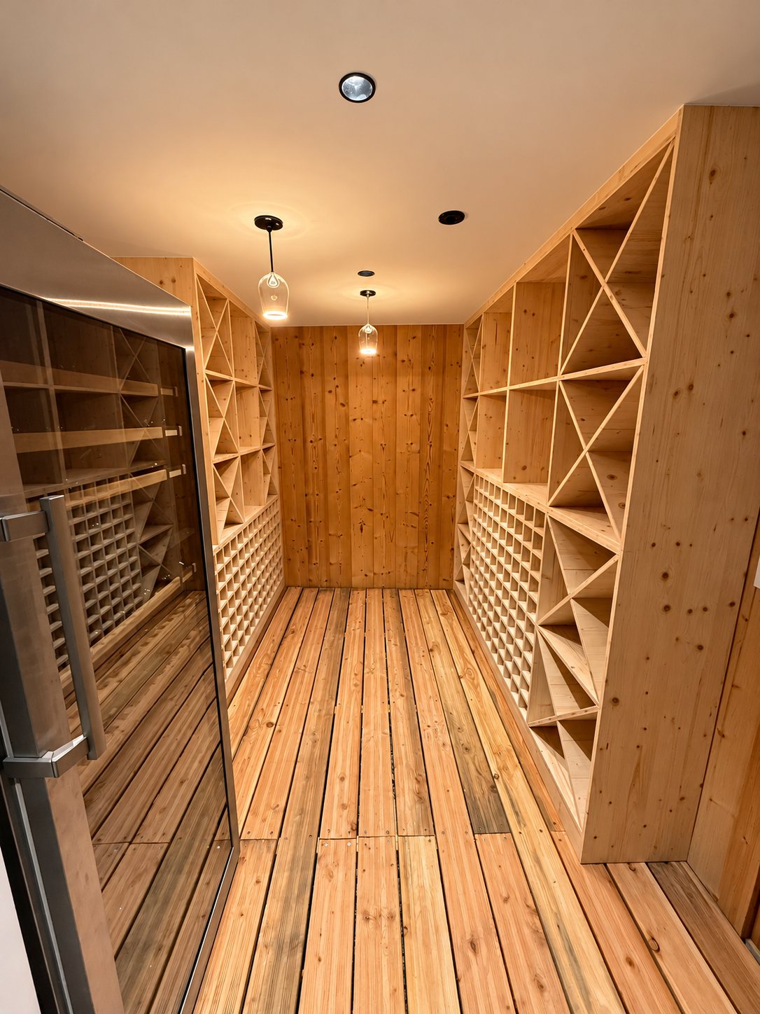 Une cave à vin aménagée en bois clair, avec casiers en croix et en alvéoles, sol en lames de bois et suspensions lumineuses.
