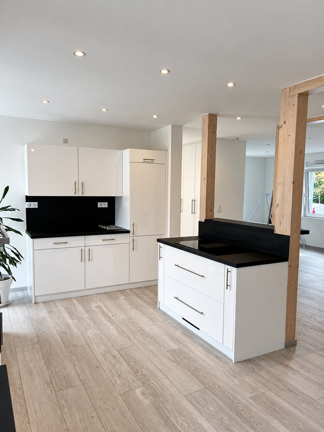 Cuisine blanche avec îlot à plan noir, parquet clair et poteaux en bois