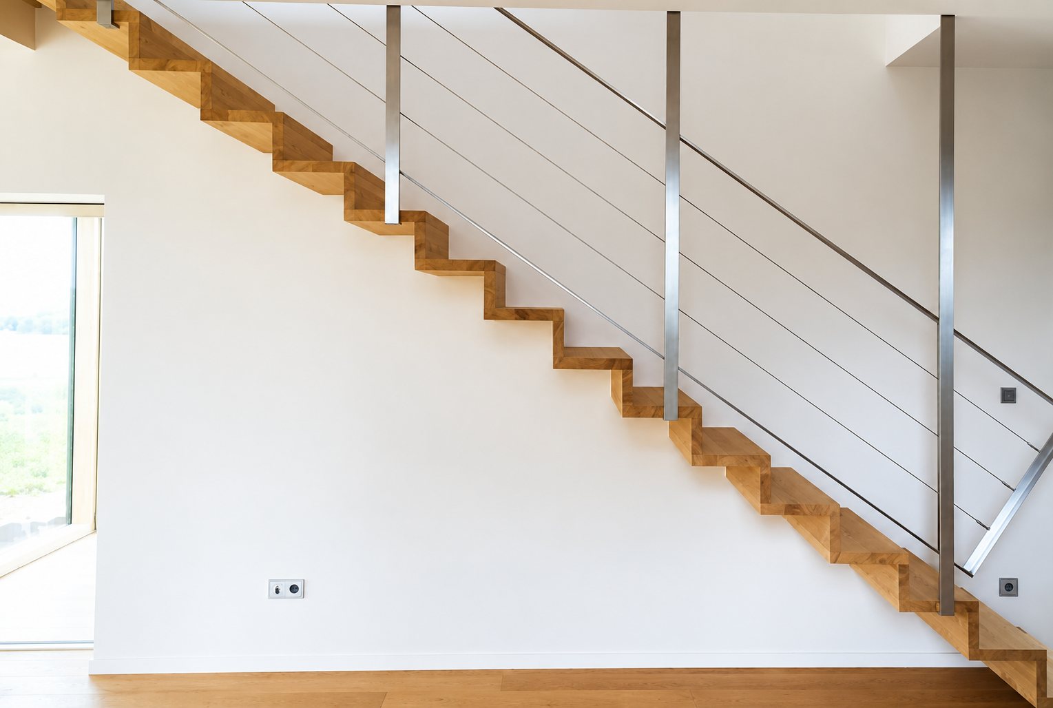 Escalier droit en bois massif à marches suspendues contre un mur blanc, avec un garde-corps en inox à câbles tendus.