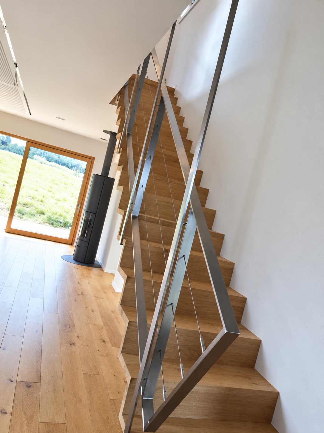 Escalier en bois avec rampe vitrée et inox, donnant sur un salon au parquet