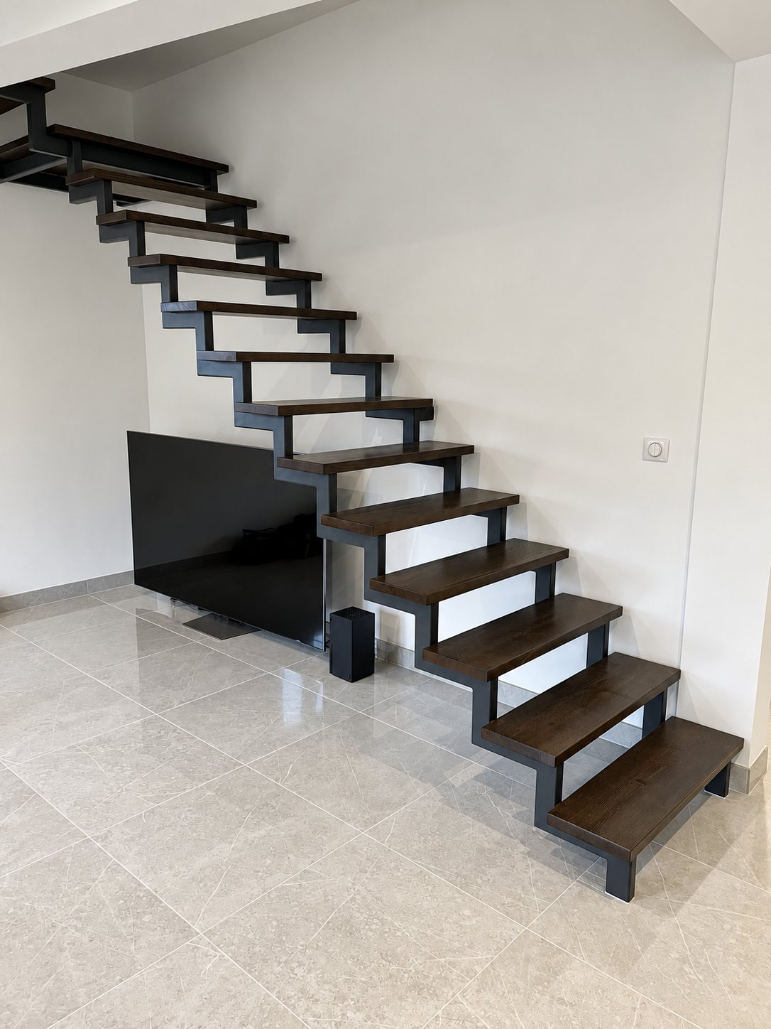 Escalier à limon métallique noir et marches en bois clair, dans un séjour lumineux
