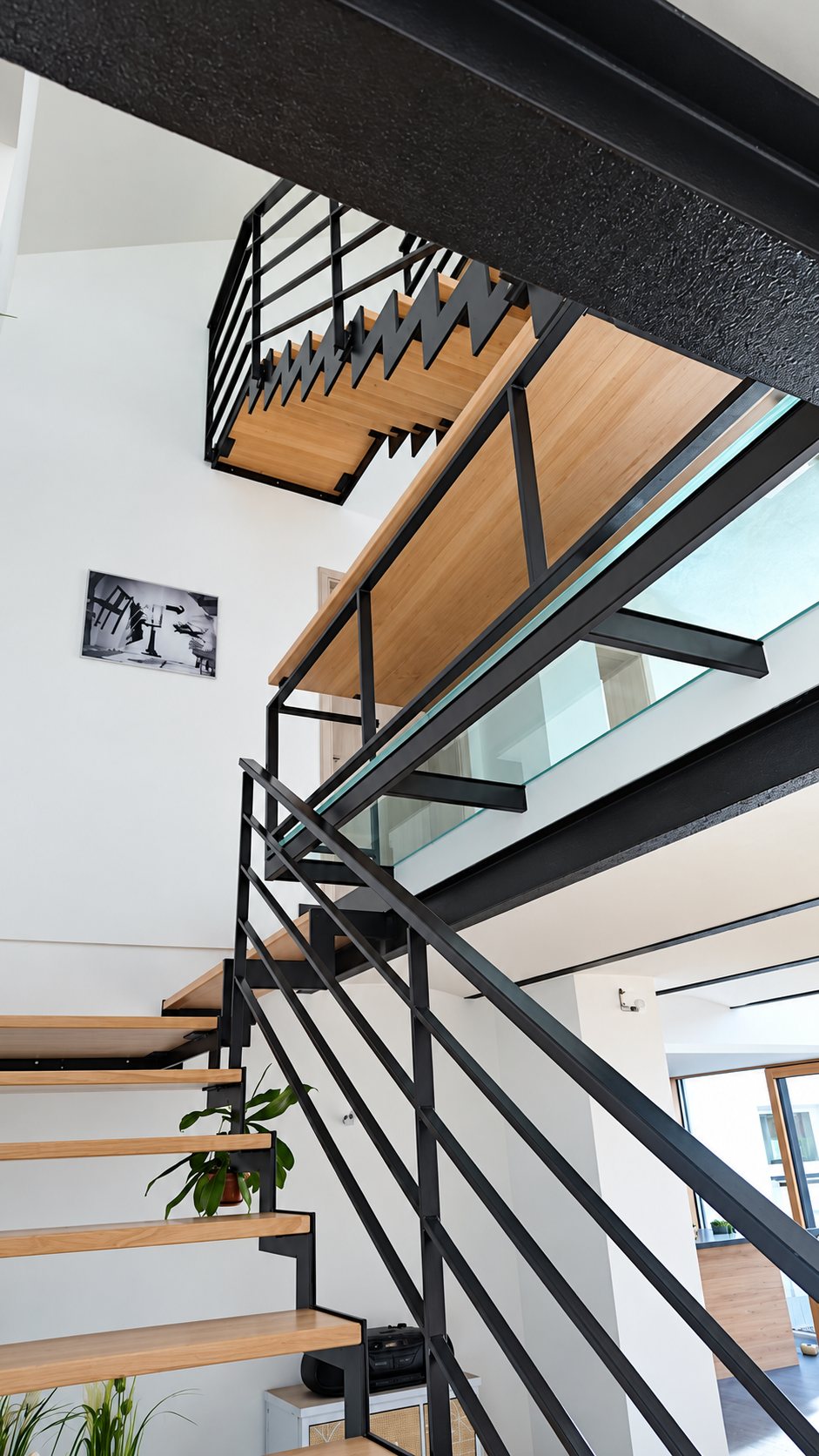 Escalier intérieur en acier noir avec marches en bois clair, garde-corps à lisses horizontales et passerelle vitrée dans une maison lumineuse.