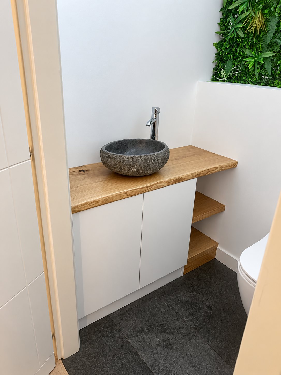 Petites toilettes avec un meuble blanc, un plan en chêne massif, une vasque en pierre naturelle, un mur végétal et un sol en ardoise sombre.