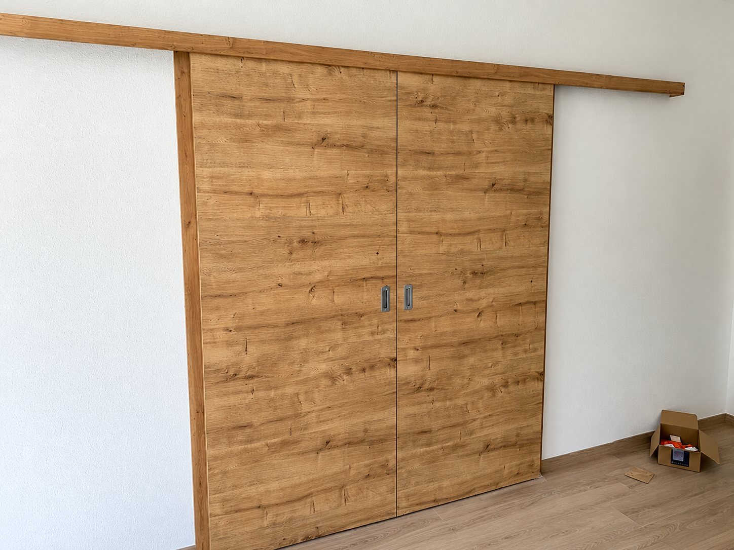 Porte coulissante double en bois sur un rail, devant un mur blanc