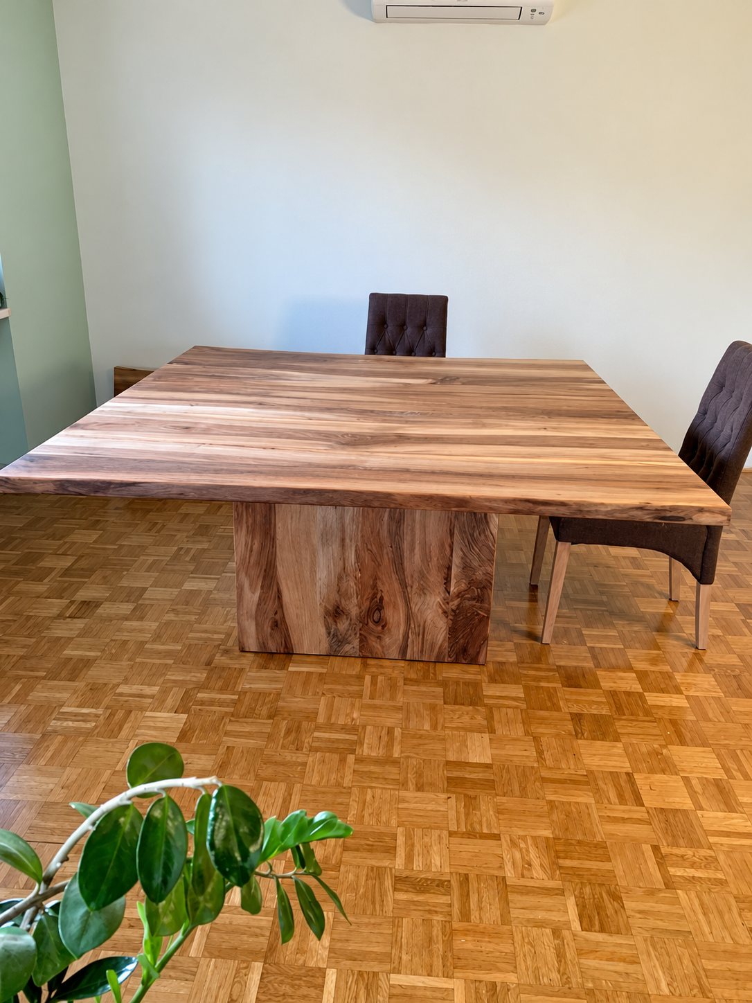 Table carrée en bois massif sur un pied central, posée sur un parquet en damier