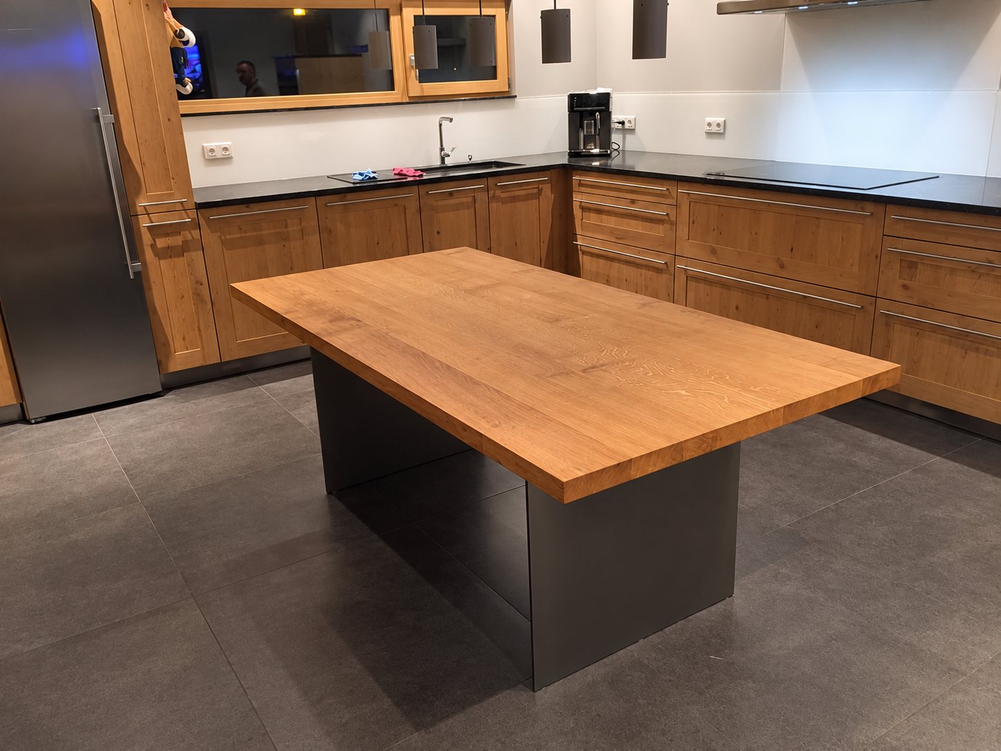 Table de cuisine en bois massif à pied sombre devant une cuisine moderne